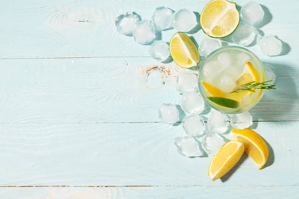 A drink of lemon and lime lemonade in transparent glasses blue background bright sunlight. Summer cocktail or mojito. - Фото, изображение