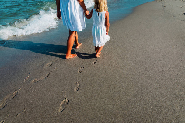 madre e hija caminando en la playa dejando huella en la arena
 - Foto, imagen