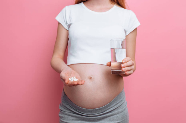水と錠剤のコップを保持している妊娠中の女性、妊娠のためのビタミン、将来の母親は赤ちゃんを期待しています - 写真・画像