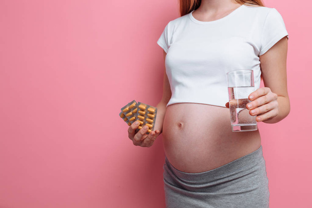 Nuoren raskaana olevan naisen käsi, jolla on läpipainopakkaus pillereitä. Vitamiinien vastaanotto raskauden aikana. pinkillä pohjalla
 - Valokuva, kuva
