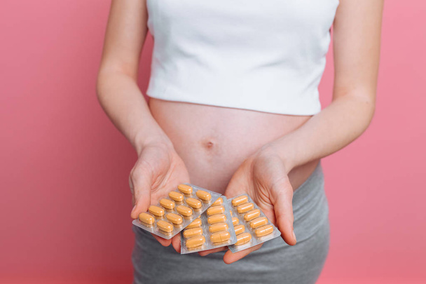 Ruka mladé těhotné ženy držící puchýř prášků. Příjem vitaminů během těhotenství. na růžovém pozadí - Fotografie, Obrázek