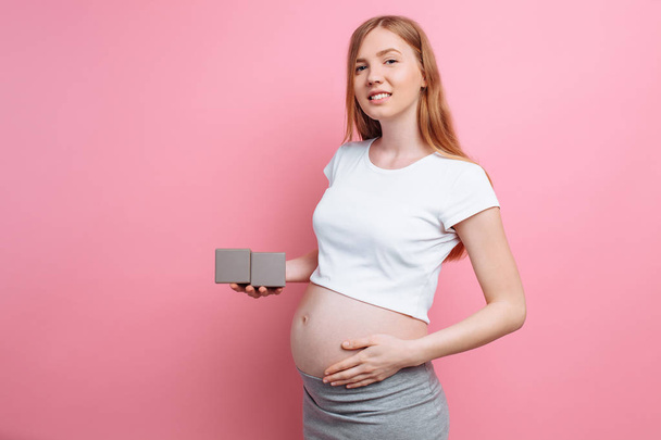Pregnant woman holding wooden cubes near the belly - Foto, Imagen