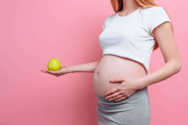 Pregnant woman holding a green apple near the belly. The concept of pregnancy, motherhood, proper nutrition - Foto, Bild