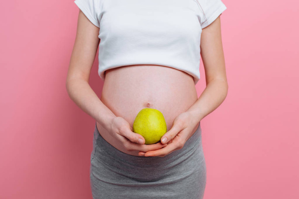 Mulher grávida segurando uma maçã verde perto da barriga. O conceito de gravidez, maternidade, nutrição adequada
 - Foto, Imagem