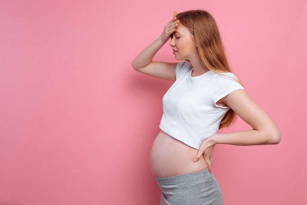 Young pregnant woman with a headache, on a pink background - Fotó, kép