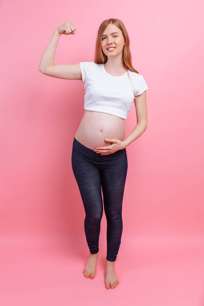 Athletic pregnant girl shows a gesture of strength - Foto, afbeelding