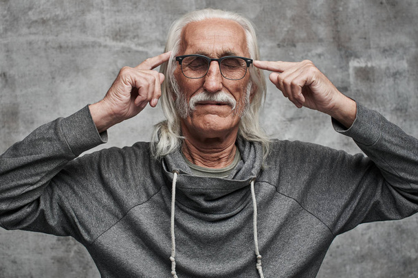 Aged gray haired Caucasian male pensioner thinks diligently, holding fingers at temples. Grandfather in glasses with mustache trying to concentrate, brainstorming, alzheimer - Φωτογραφία, εικόνα