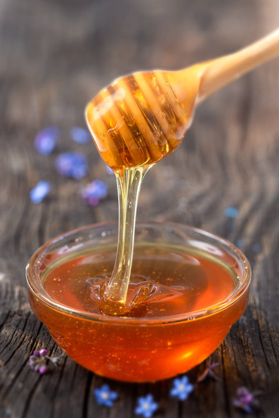 Honey pouring from stick to the bowl wooden background - Photo, Image