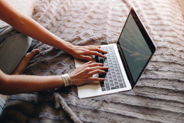 Vrouw handen typen op laptop toetsenbord in de gezellige slaapkamer - Foto, afbeelding