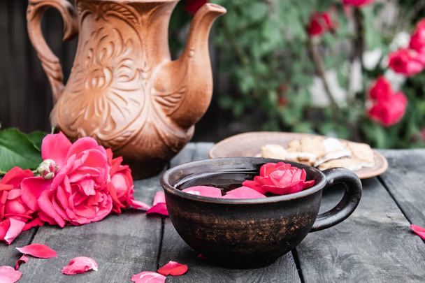 Tea from rose petals in a cup on a wooden rustic background against the background of a rose bush. - Photo, Image