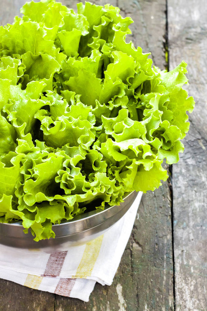 Fresh lettuce leaves in metal bowl on old wooden table - Photo, Image
