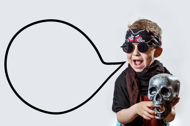 un niño rockero en gafas negras, bufanda, bandana y con un cráneo en las manos sobre un fondo claro
 - Foto, Imagen