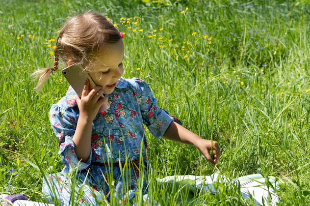Happy little girl talking on the phone on the green lawn. - Фото, зображення