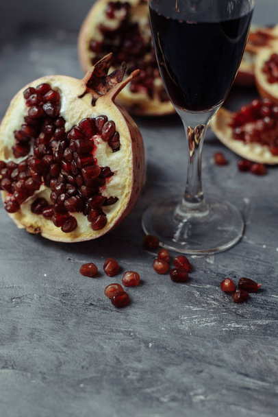 Una copa de vino con vino tinto se encuentra sobre un fondo gris grunge junto a las granadas. Frutas y vino de granada
 - Foto, imagen