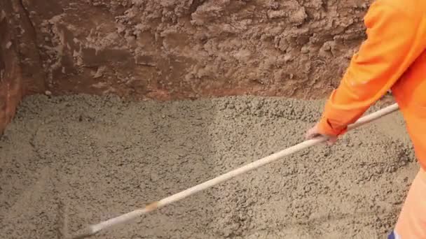 Trabalhador está nivelando concreto após o luto. Mason está usando ancinho para espalhar concreto fresco na trincheira quadrada
. - Filmagem, Vídeo