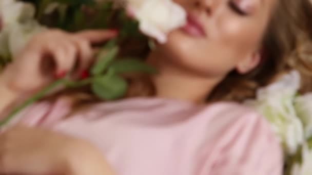 fashion video of beautiful young woman with long blond hair in elegant silk lingerie posing with flowers - Filmati, video