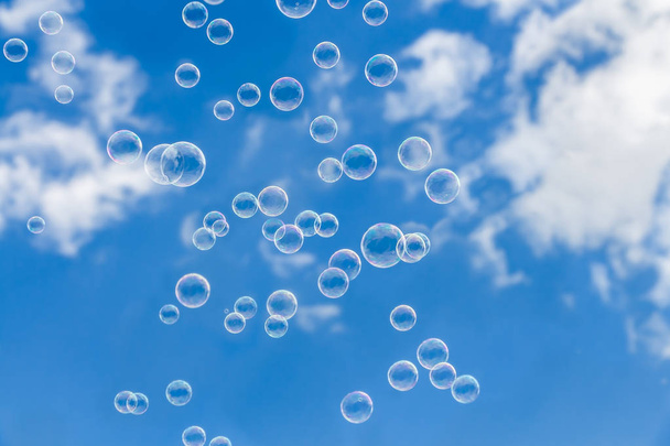 Um grupo de bolhas de sabão transparente arco-íris no céu azul com fundo de nuvens brancas
 - Foto, Imagem