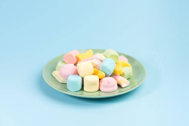 Green plate with marshmallow isolated on blue background. - Фото, зображення