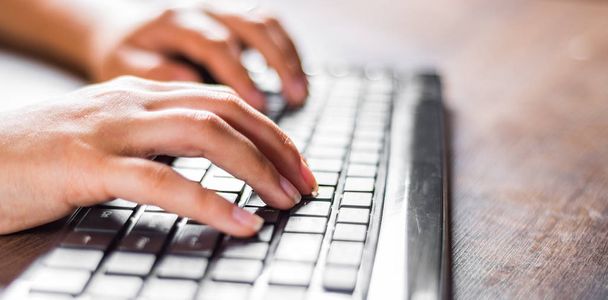 Woman working at home office hand on keyboard close up on wooden table background - Photo, image