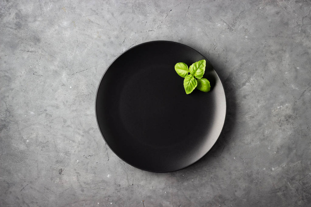 Table setting. Black plate and basil leaves over gray concrete background. - Valokuva, kuva