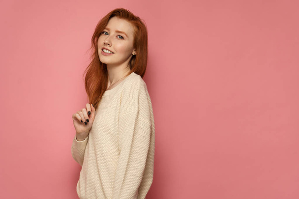 Redhead girl stands sideways to the camera, touches her hair and - Foto, afbeelding