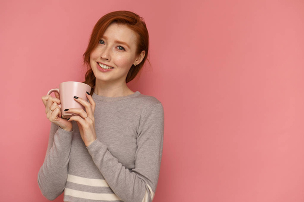 Redhead young woman with a cup smiles looking at camera - Photo, Image