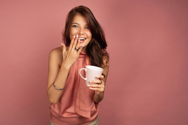 Young dark-haired woman with pink cup in her hand tries to cover - Photo, Image