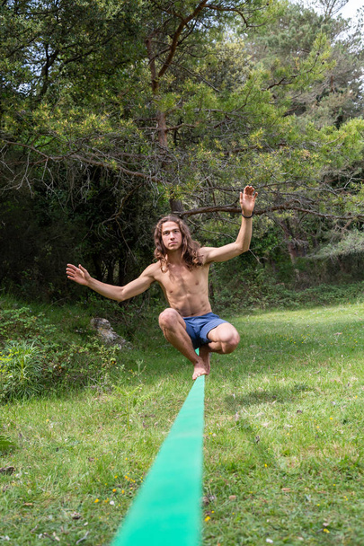 Jeune homme actif avec torse nu équilibrant sur slackline dans le champ vert en été
 - Photo, image