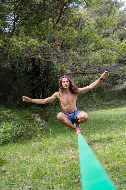 Active young man with naked torso balancing on slackline in green field on summertime - 写真・画像