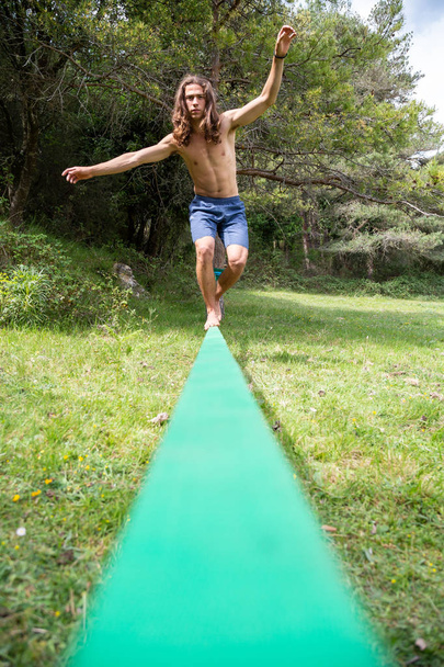 Joven activo con torso desnudo balanceándose en slackline en campo verde en verano
 - Foto, imagen