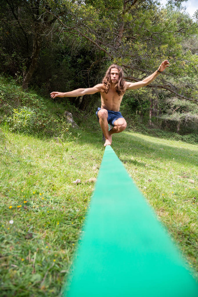 Active young man with naked torso balancing on slackline in green field on summertime - Photo, Image