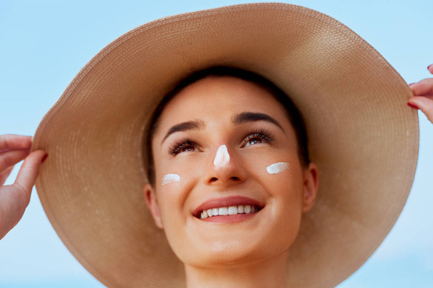 Beauty Woman smile applying sun cream on face. Skin care. Body Sun protection. sunscreen. Female in hat smear moisturizing lotion on skin - Фото, изображение