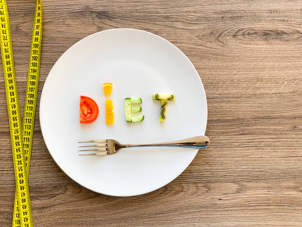 Word DIET made of sliced vegetables in plate with measuring on wood background - Zdjęcie, obraz