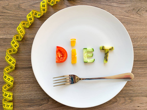 Word DIET made of sliced vegetables in plate with measuring on wood background - Photo, Image