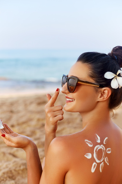Gyönyörű nő mosoly alkalmazása napkrémet az arcon. Bőrápoló. Body napvédő. Fényvédő. Női kalap kenet hidratáló krém a bőrön - Fotó, kép