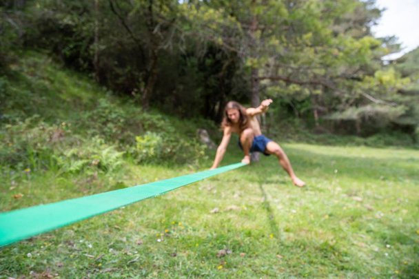 Defocused young man with naked torso doing slackline in field on summer day - Photo, Image