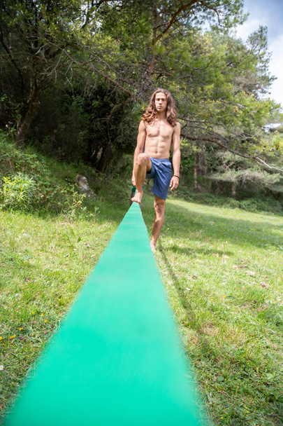 Hombre joven desenfocado con torso desnudo haciendo slackline en el campo en el día de verano
 - Foto, Imagen