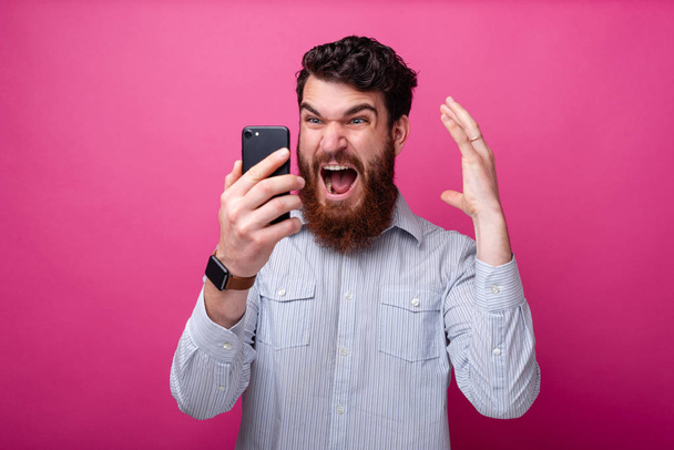 young bearded man shocked looking at his phone gesturing. - Photo, Image