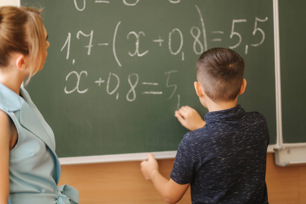 Young female teacher help schoolboy. Boy stand by the blackboard - Photo, Image