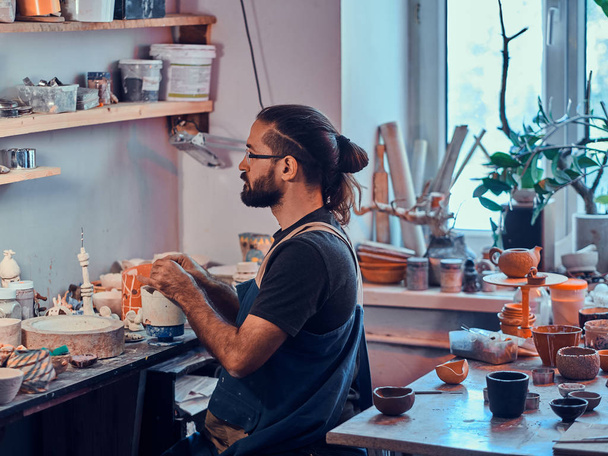 Entusiastici Potter in glazen in zijn eigen atelier is workig op een nieuwe handgemaakte theepot. - Foto, afbeelding