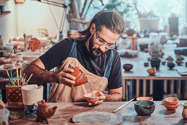 Прилежный привлекательный мужчина кладет красочную глину в свой новый горшок ручной работы
. - Фото, изображение