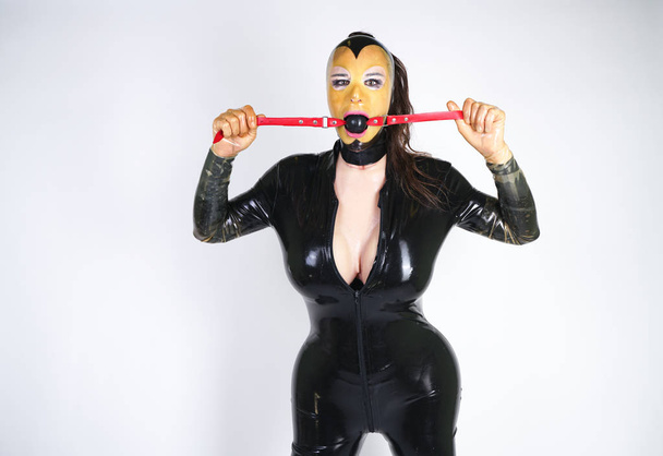 гаряча пишна трансвестит одягнена в латексну гумову маску і чорний фетиш костюм. дивна людина з бдсм кляпом у руках сексуально грає
.  - Фото, зображення