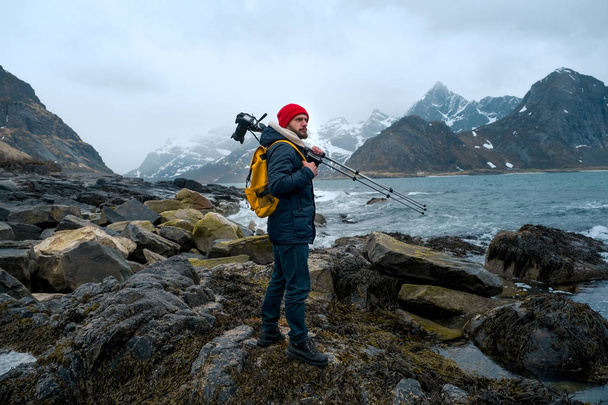 Jovem fotógrafo de pé na rocha nas montanhas na praia fotografando as paisagens nas ilhas Lofoten, na Noruega
. - Foto, Imagem
