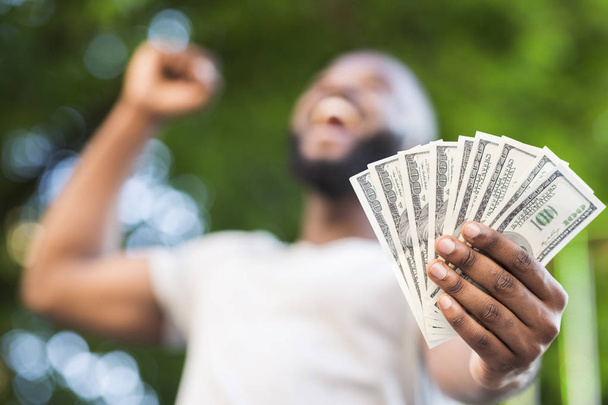 Happy african american man holding fan of dollars in hand - Фото, изображение