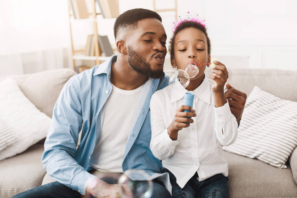 Afro papá y hija soplando burbujas de jabón
 - Foto, imagen