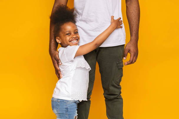 彼女の大きな父親、オレンジのスタジオの背景を抱きしめる愛らしい小さな黒人の女の子 - 写真・画像