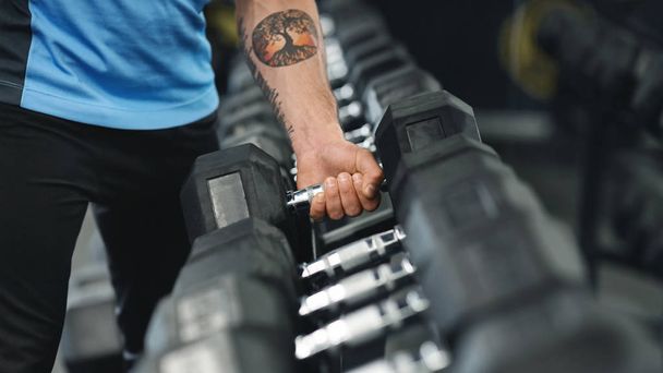 Brazo masculino muscular recogiendo pesadas mancuernas del rack del equipo
 - Foto, imagen