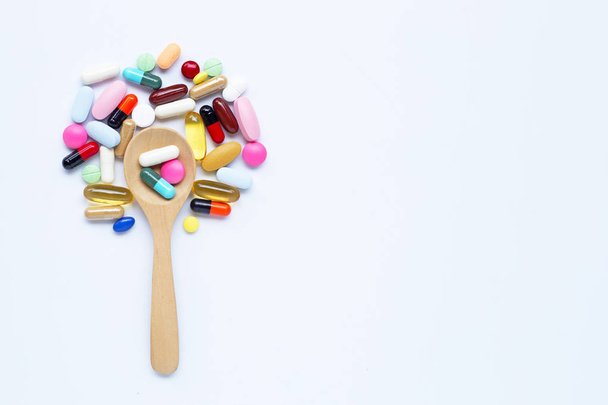 Comprimidos coloridos, cápsulas y pastillas con cuchara de madera sobre blanco
 - Foto, imagen