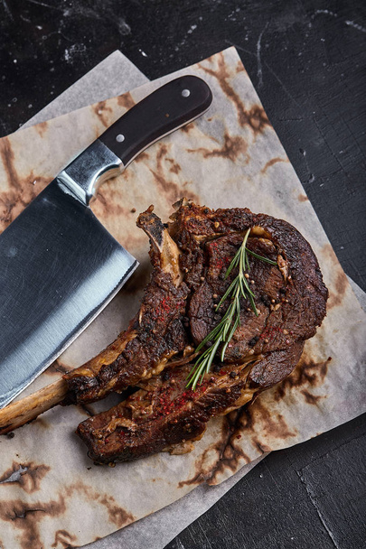 Biftek Tomahawk se zeleninou a nožem na stole. Grilované maso s grilovanou zeleninou a čerstvou zeleninou na stole. - Fotografie, Obrázek