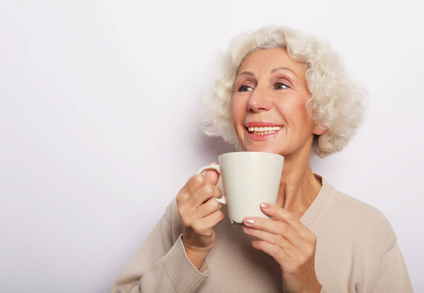 old excited lady smiling laughing, holding cup drinking coffee, tea, over white background - Foto, Imagem